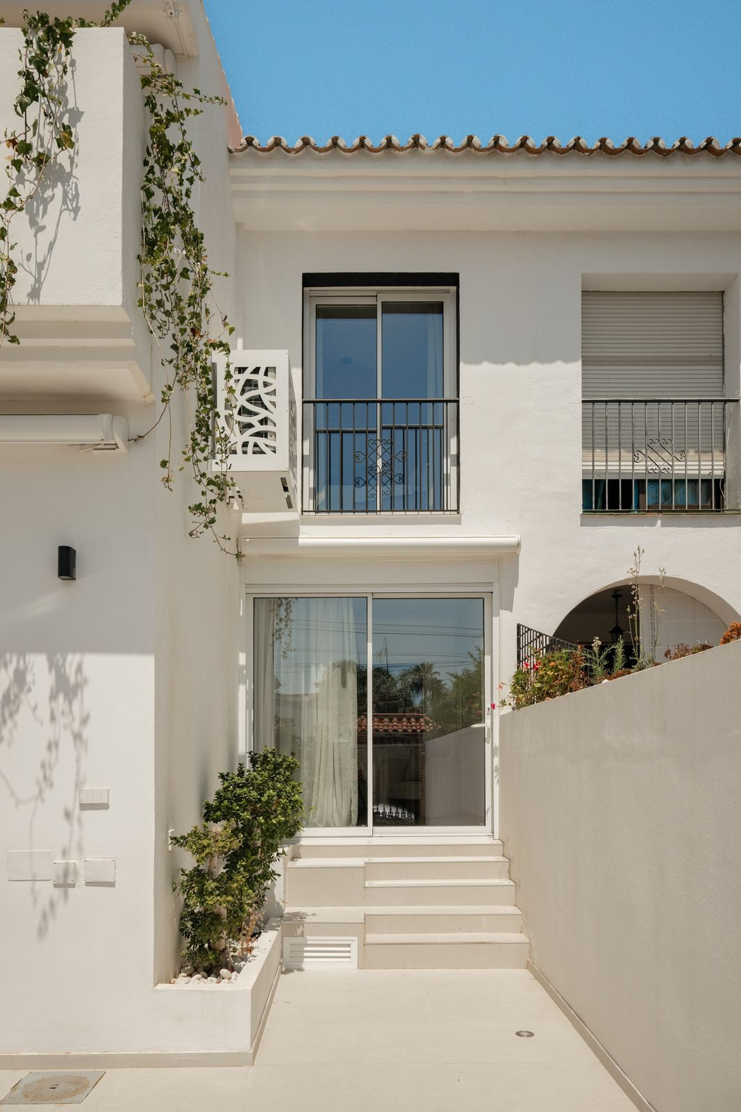House facade with sliding door, balcony and climbing plant seen from the patio