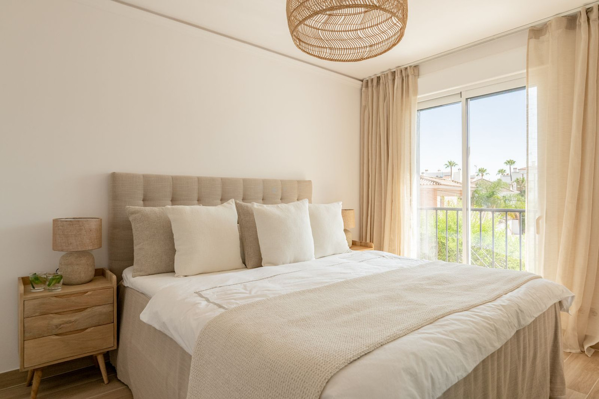 Bedroom with double bed and balcony door with view of palms and tiled roofs