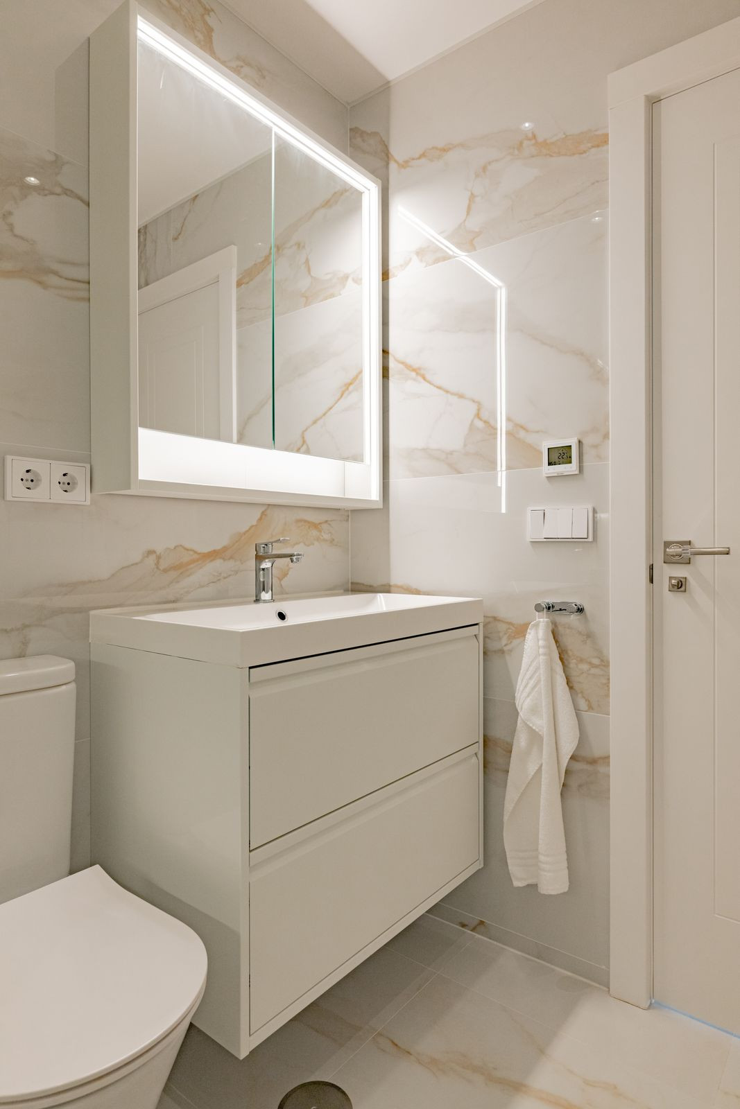 Bathroom with double basins, illuminated mirror cabinet and marble walls